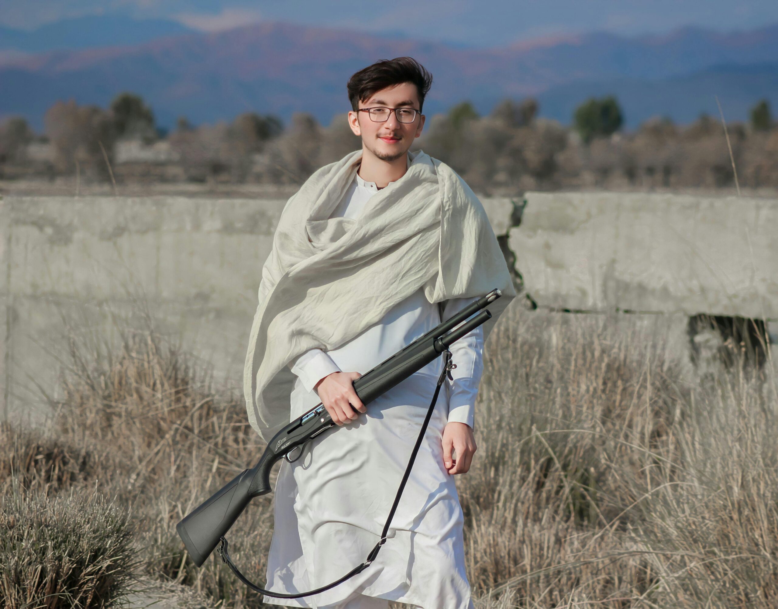 Young man wearing traditional Pakistani clothing holding a gun outdoors in Khyber Pakhtunkhwa.